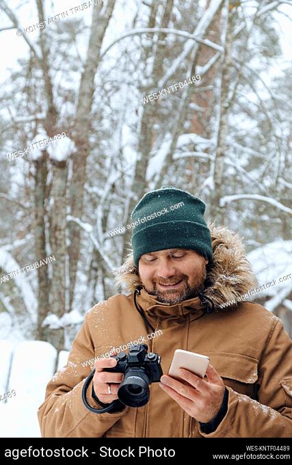 Portrait of relaxed man with digital camera and mobile phone in winter forest