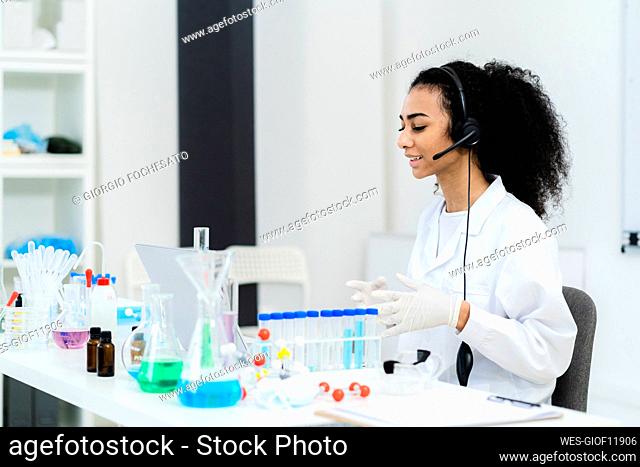 Young female researcher talking on video call through laptop in laboratory