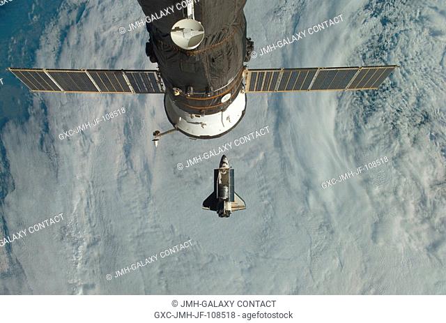 Backdropped by a cloud-covered part of Earth, Space Shuttle Discovery (STS-120) approaches the International Space Station during STS-120 rendezvous and docking...