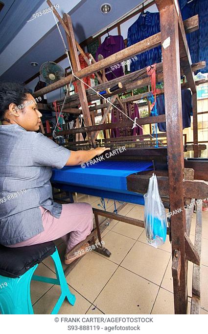 A woman working a manual loom, making cloth for Balinese clothes in Ubud, Bali