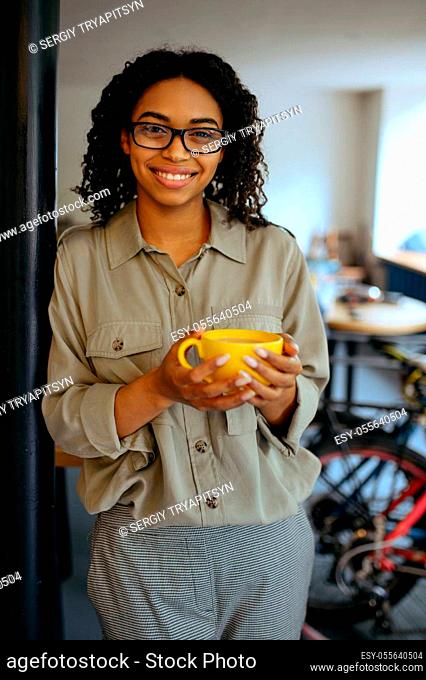 Pretty female student in glasses poses with cup of coffee and using a phone in cafe. Woman learning a subject in coffeehouse, education and food