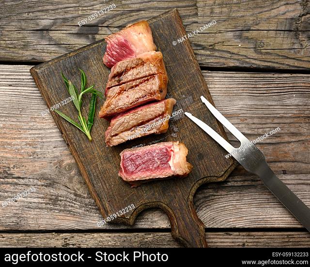 sliced fried beef steak New York striploin on a wooden cutting board, degree of doneness rare, top view