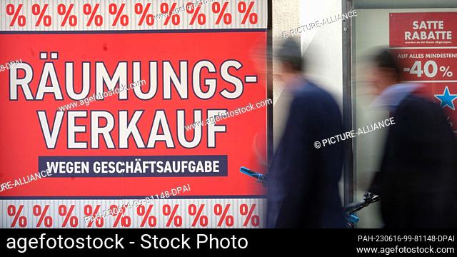 16 June 2023, Baden-Württemberg, Stuttgart: Two men walk past a retail clothing store in downtown Stuttgart with a banner that reads ""Clearance sale due to...