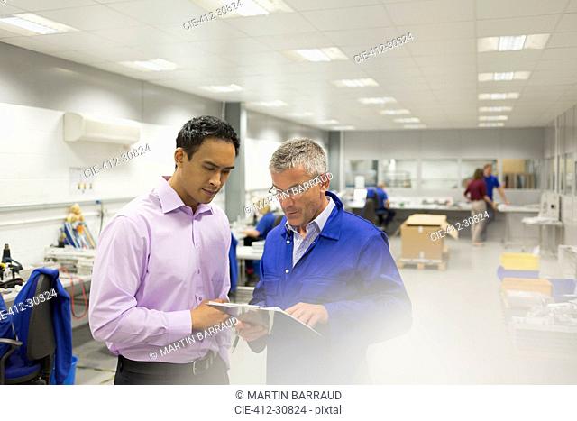 Manager and engineer looking at clipboard in steel factory office