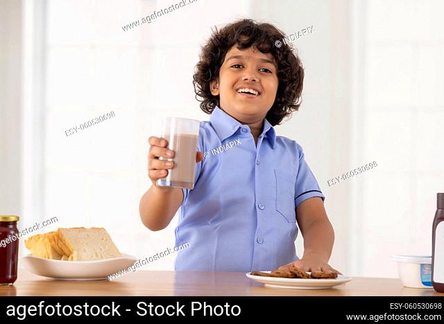 A boy happily showing a glass of milkshake in front of camera