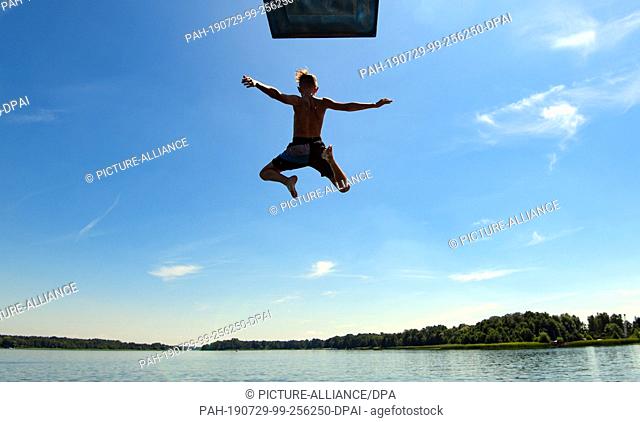 24 July 2019, Brandenburg, Storkow: A boy jumps from the three-meter tower at the lido into the water of Lake Storkow. Photo: Patrick Pleul/dpa-Zentralbild/ZB