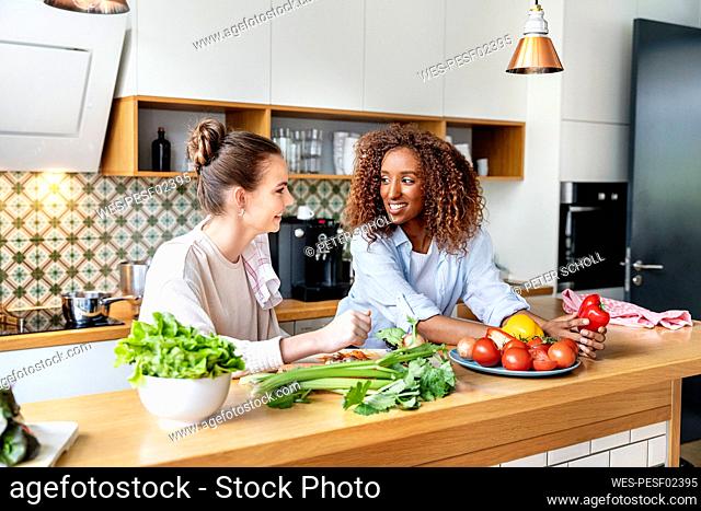 Smiling female coworkers looking at each other while leaning on counter in office kitchen