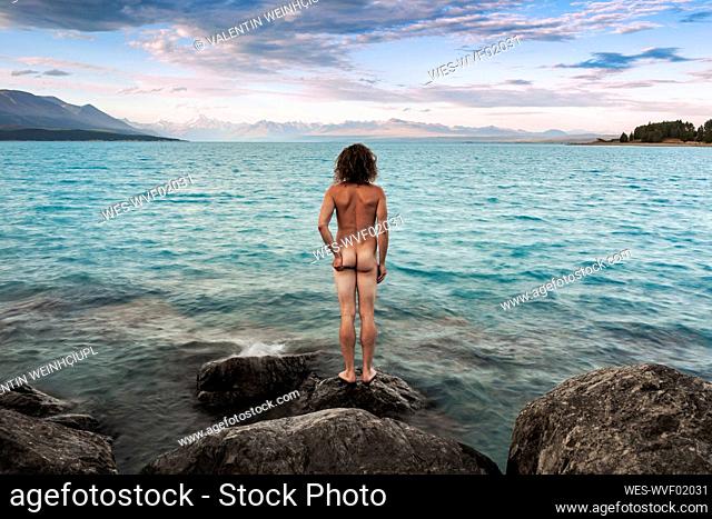 New Zealand, Canterbury, Rear view of naked man looking at Lake Pukaki at sunset