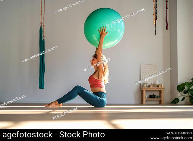 Woman exercising with fitness ball sitting in yoga studio