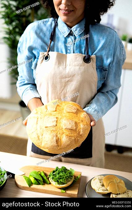 Mid section of young woman holding freshly baked loaf of bread