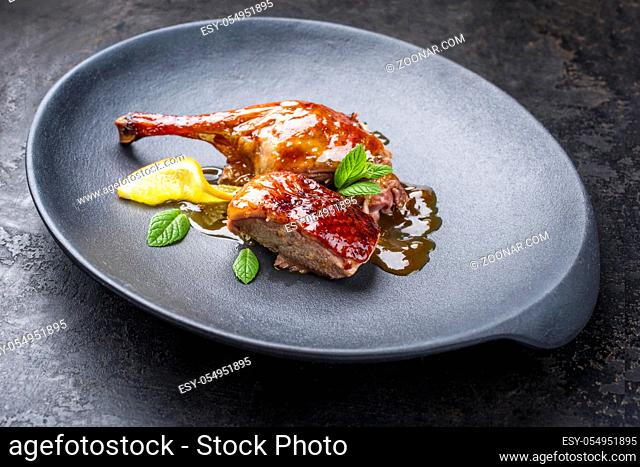 Traditional roasted Christmas duck breast and leg with orange slice and herbs as closeup on a modern design plate