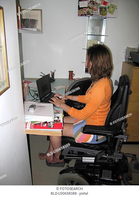 Young woman uses electric wheelchair to access a computer workstation