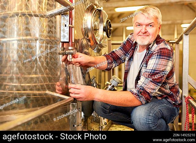 Mann als Winzer in einer Weinkellerei kontrolliert frischen Wein am Gärtank