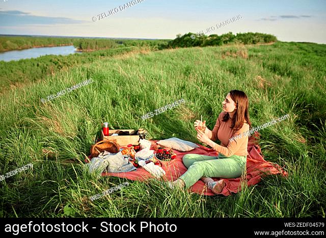 Young woman having infused water and looking at river in field