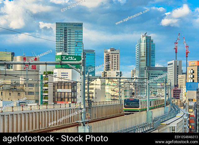 kanda station where the trains of the yamanote line pass between the top of the buildings of the district of Chiyoda under the blue sky of Tokyo