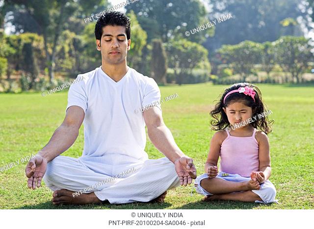 Man meditating with his daughter in lawn, Gurgaon, Haryana, India