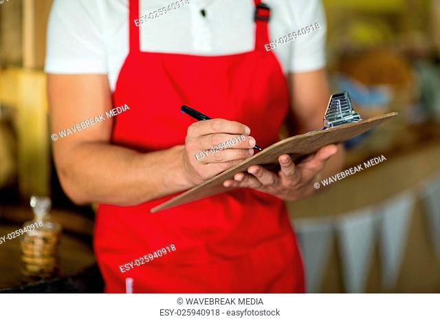 Mid section of bakery staff writing on clipboard at counter