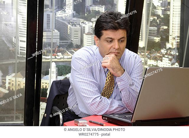 Executive looking at screen of laptop with worried expression in office at top floors of skyscraper in modern city MR 687U