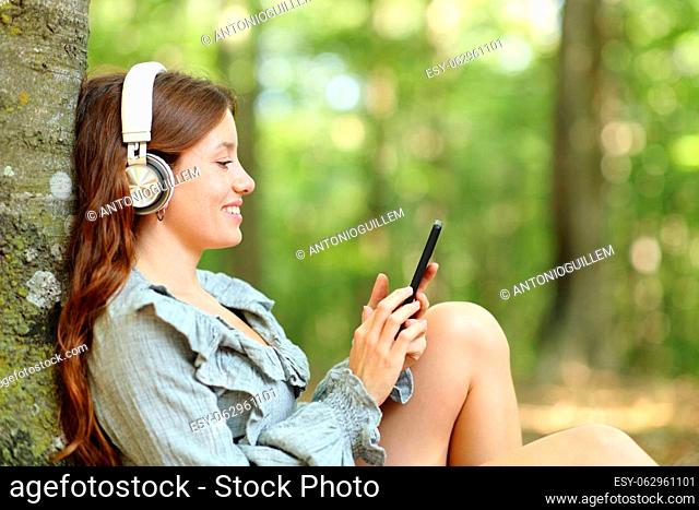 Profile of a happy woman listening to music with headphones and smartphone relaxing in a forest