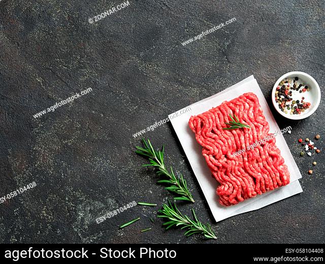 Fresh raw minced beef on backing paper and cutting board and ingredients over black cement background with copy space. Top view or flat-lay