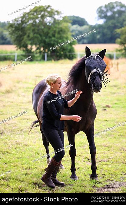 PRODUCTION - 15 July 2022, Schleswig-Holstein, Schmedeswurth: Sophie Graf, horse trainer, adjusts the fly guard on the horse ""Chico""