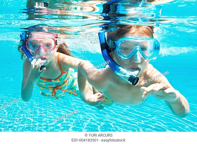 Portrait of two children a boy and a girl submerged in a pool wearing snorkels
