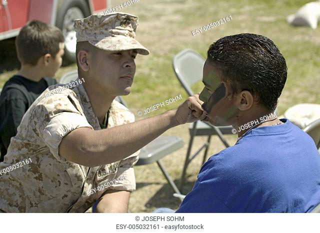 Army solider applying camouflage to young boy at the 42nd Naval Base Ventura County NBVC Air Show at Point Mugu, Ventura County, Southern California