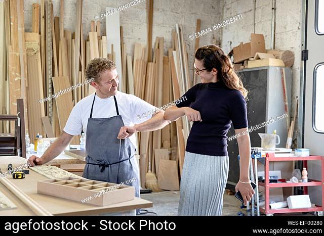 Smiling man and woman giving elbow bump while standing at workshop