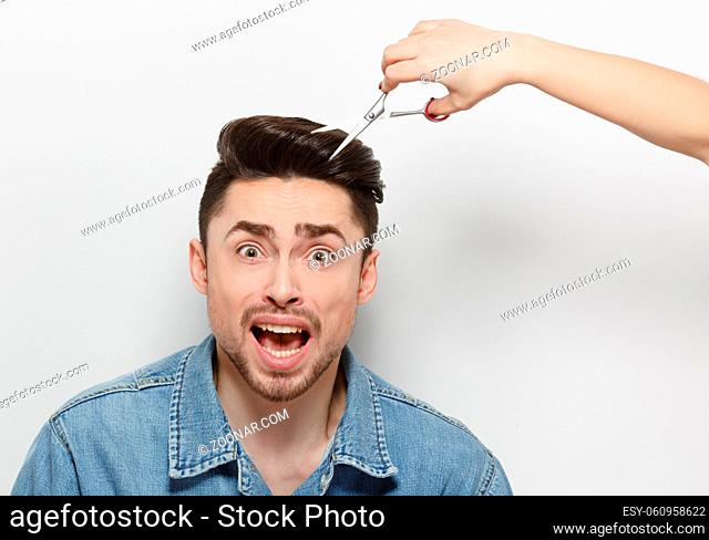Portrait of frightened handsome man having haircut over white background. Man with black hair sitting in studio