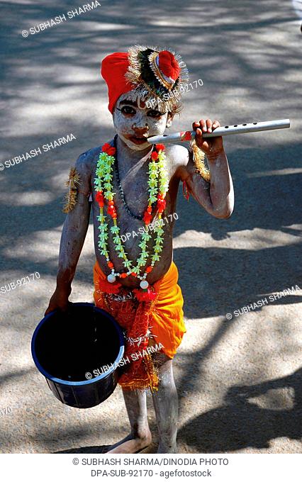 Indian child begging, dressed as Lord Krishna with flute and garland , india