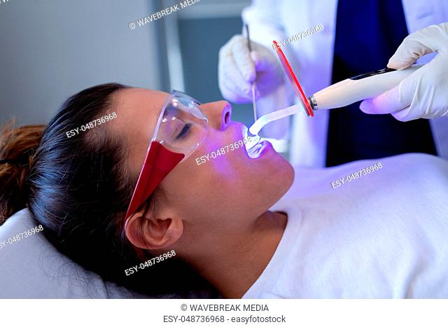 Female dentist examining patient with dental curing light in clinic