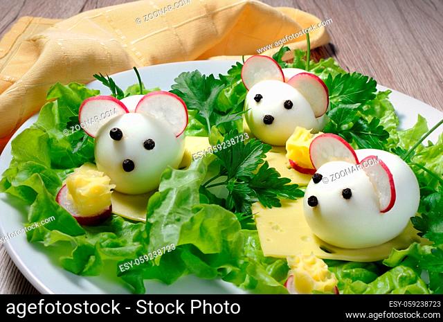 Serving a festive children's snack, boiled eggs in the form of mice in lettuce leaves and cheese cubes