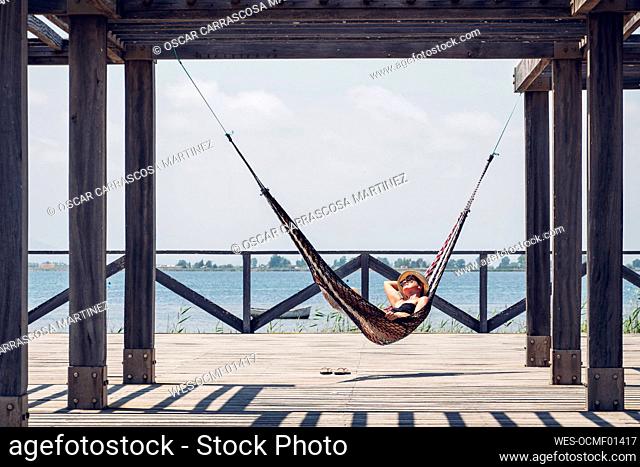 Relaxed woman lying in hammock hanging from metallic structure on boardwalk