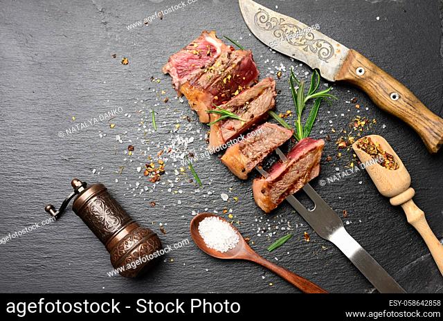 sliced fried beef steak on a black background with spices, degree of doneness rare, top view