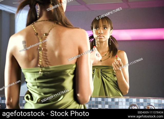 African woman holding lipstick and looking in mirror