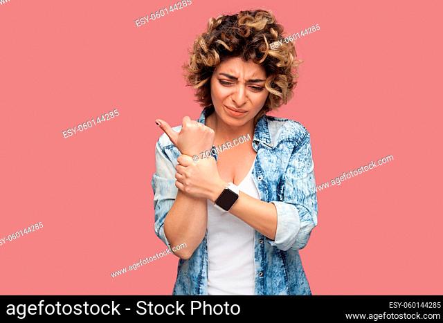 hand or wrist pain. Portrait of sick young woman with curly hairstyle in casual blue shirt standing and holding her painful hand