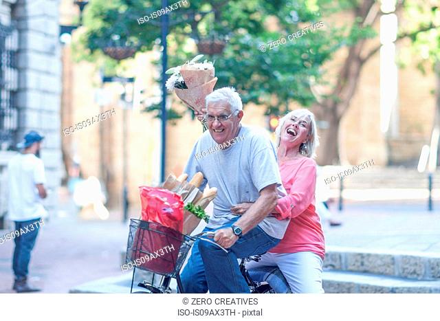 Senior man and woman holding up bouquet cycling in city