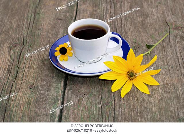 the cup of coffee on a wooden table decorated with two yellow flowers, a still life, a subject fall