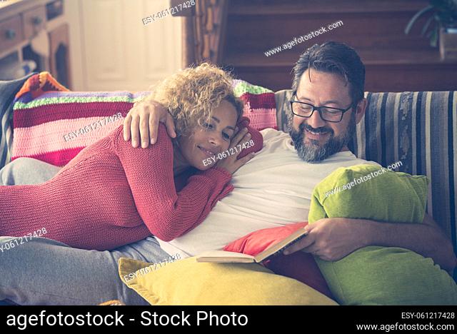Couple reading a book relaxing on sofa at home. Loving couple spending leisure time together at home. Happy man reading a book to his wife relaxing in the...
