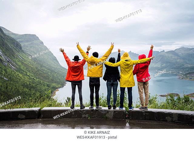 Norway, Senja island, rear view of cheering friends standing on an observation point at the coast