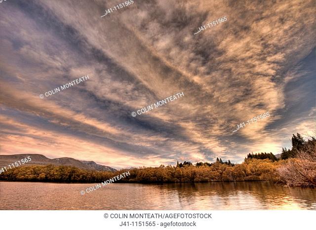 Frontal weather system from SW moves high over Lake Heron sheep & cattle station at dawn, autumn, Canterbury