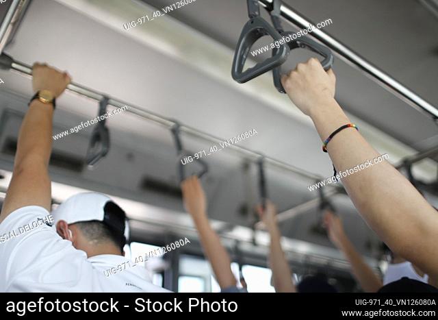 Hands holding the handle in tram, train, bus or subway. Passenger standing in public transportation. Person commuting. Commuter going to work. Hoi An