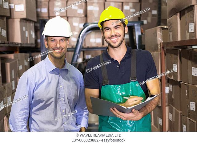 Warehouse manager and foreman smiling at camera in a large warehouse