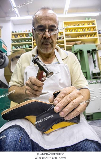 Shoemaker working with hammer on shoe in his workshop