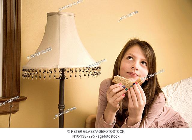 Preteen girl eating a sandwich in her bedroom