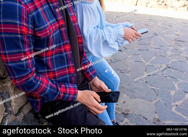 Trendy unrecognizable young modern people sending messages with technology phone internet connected - cellular people addiction concept - couple with smartphone