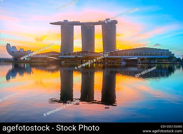 Morning in Singapore. Three buildings of the hotel in the form of a ship are reflected in the calm water of Marina Bay. The rising sun painted the sky in orange...