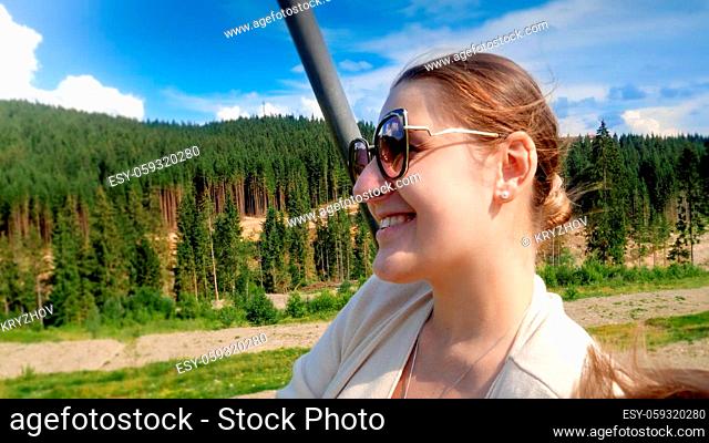 Portrait of happy smiling young woman enjoying ride on ski lift on summer day at mountains. Concept of travel and tourism in mountain at summer