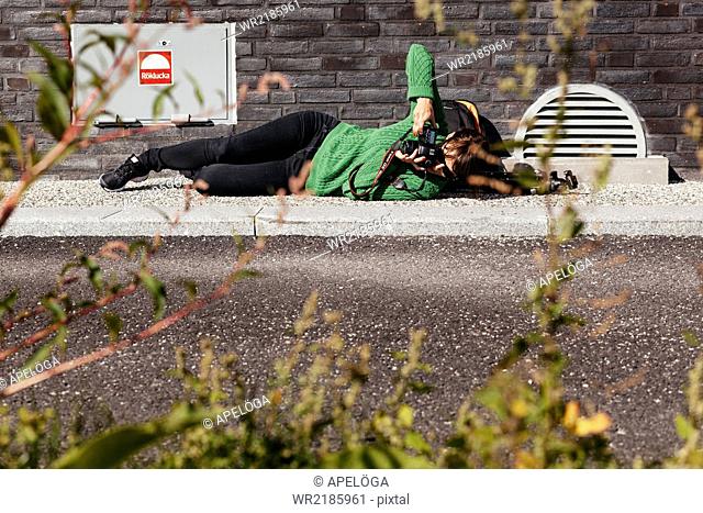 Full length of woman photographing while lying on sidewalk