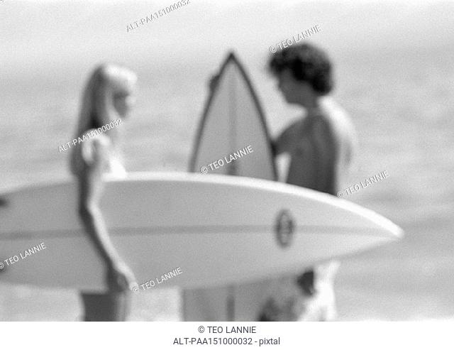 Couple holding surfboards, talking, blurred, b&w
